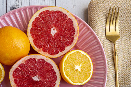 Delicious grapefruits and oranges for breakfast with coffee and golden silverware on a pink plate.の写真素材