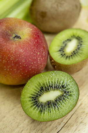 Close-up of kiwi cut in half and more kiwis in the background with red apple on light wooden backgroundの写真素材