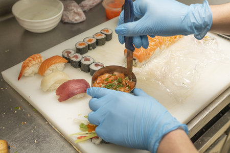 A chef disassembling a salmon tartare with chives next to some Japanese nigiri pieces and maki piecesの写真素材