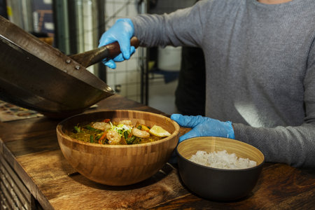 An Asian chef preparing a bowl of ramen with prawns, pumpkin noodles and a small bowl of white riceの写真素材