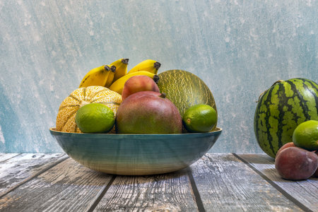 Blue bamboo tray with fresh seasonal fruits. Piel de sapo melons, mangoes and ripe bananas, peaches and watermelons.の写真素材