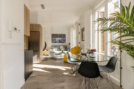 Living room of studio apartment with open kitchen with round glass table, black resin chairs and...
