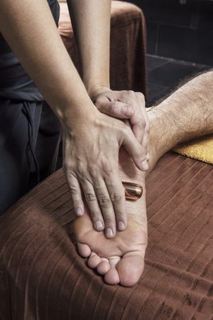 Applying a relaxing massage with metals on the soles of a patient's feetの写真素材