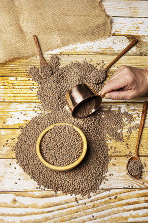 Still life with dumped bulk dried lentils on a table and a copper june meter with a bamboo wooden bowl and a hand pouring the materialの写真素材