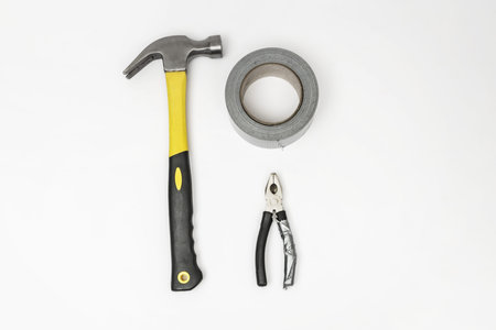 A pair of pliers, a roll of gray adhesive tape and a carpenter's hammer on a white surface