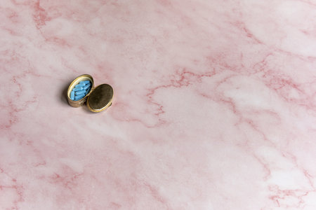 A small metal box used as a pill box on a pink marble surfaceの写真素材
