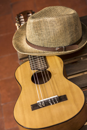 A guitar resting on a wooden box and a straw hat and clay flooringの写真素材