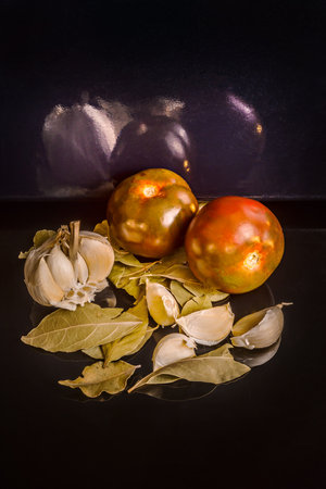 A few ripe tomatoes with a head of garlic on bay leavesの写真素材
