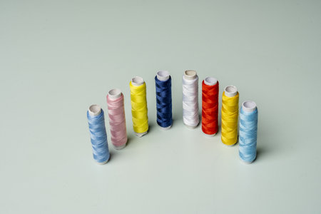A group of spools of multicolored thread arranged vertically on a smooth pastel blue surfaceの写真素材