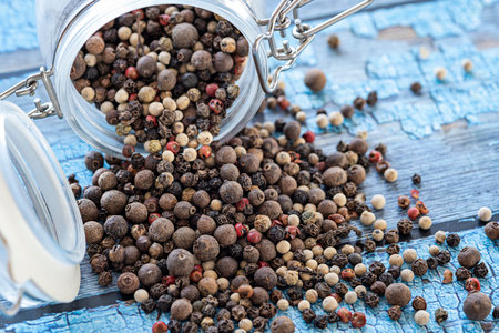 Kernels of various types of volcanic peppers from a jar on a blue table