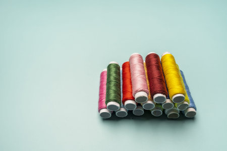 Spools of brand new multicolored sewing thread stacked pyramidally on a turquoise blue surface