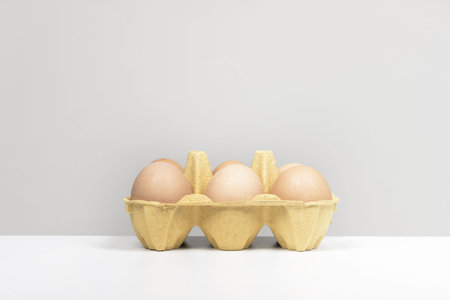 A carton of half a dozen brown eggs on a smooth white surface