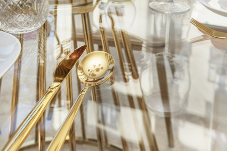 Golden cutlery on a glass table along with glasswareの写真素材