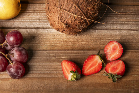 Some delicious ripe strawberries cut in half, together with grapes on a plank tableの写真素材