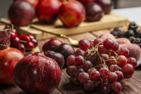 Some pomegranates wet with drops of water along with another large number of fruits of similar tones, bunches of grapes and forest fruitsの写真素材