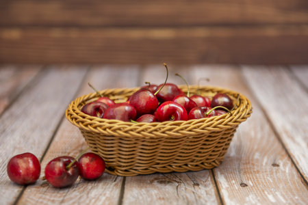 Delicious ripe cherries inside a small wicker basket on a wooden plank surface that begs you to eat themの写真素材