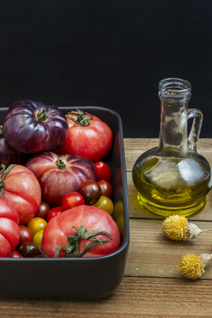 A still life with a tray full of tomatoes of various kinds and a container of olive oil on an untreated wooden tableの写真素材