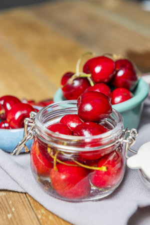 some ripe canned cherries in a clear glass jar with a lid next to a small blue porcelain saucepanの写真素材