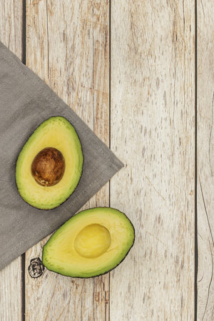 A ripe avocado cut in half on a gray cloth and a light colored wooden plank table