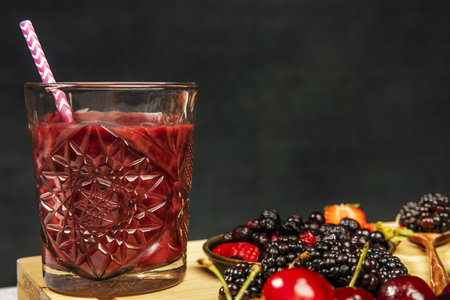 Red fruit detox juice in cut glass with a straw next to some ripe blackberries and cherriesの写真素材