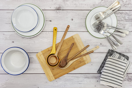 A still life photo seen from the top with wooden spoons, metal forks and some enameled metal plates