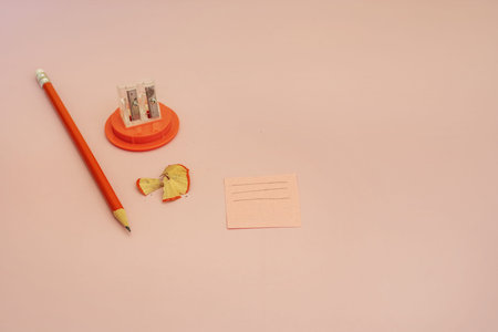 A sharpened orange pencil with a small eraser on one end next to a pencil sharpener, a note and wooden peelsの写真素材