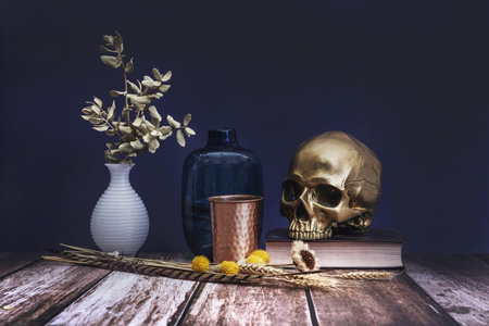 A still life with a dominant golden skull over a book along with dried plants and containersの写真素材