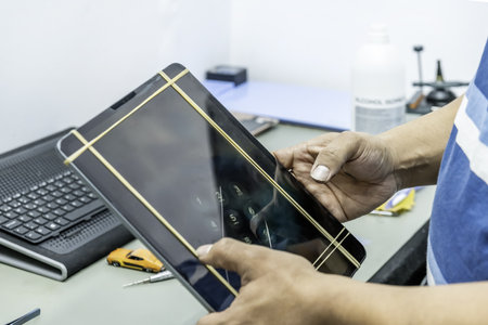 A technician repairing the screen of a large, thin tablet in his electronics workshopの写真素材