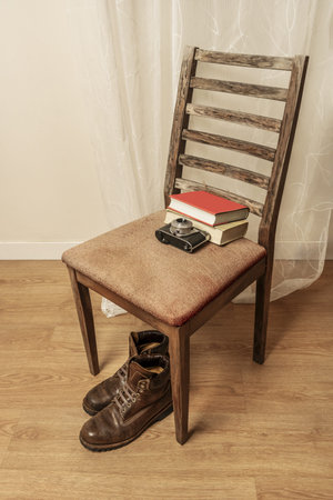 Brown leather boots next to an antique camera and some books on an old upholstered chair
