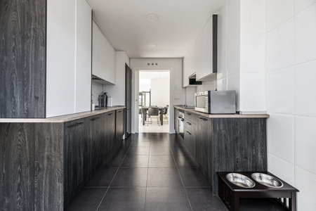 Large kitchen furnished with integrated black and white wooden furniture and access to a bright living room with a black wooden tableの写真素材