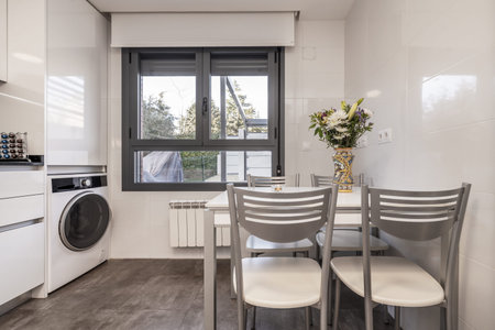 White dining table with metal chairs in the kitchen of a two-story house with lots of appliancesの写真素材