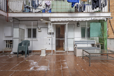 Inner courtyard of a house with dark terracotta floors, an aluminum Libyan fence, some scattered furniture and balconies with clothes hanging on the upper floorsの写真素材