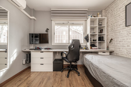 Youth bedroom with single bed with study table with white drawers, mirror on the wall, aluminum window and black swivel armchairの写真素材