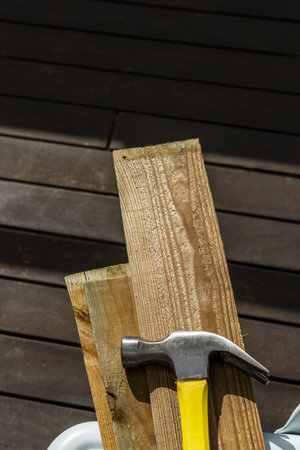 A metal hammer with a yellow and black wooden handle on several planks of thin unvarnished wood on a...