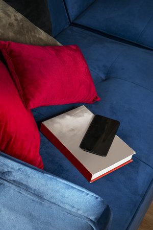 A blue velvet sofa with a book and a mobile phone on the seatの写真素材