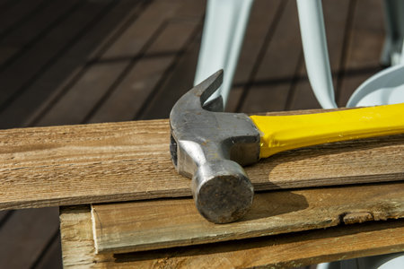 A metal hammer with a yellow and black wooden handle on several planks of thin unvarnished wood