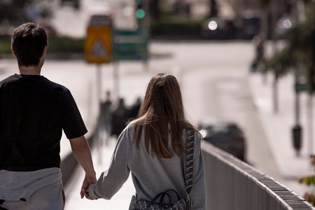 A couple walking hand in hand across a modern pedestrian bridge, contemporary architecture framing...