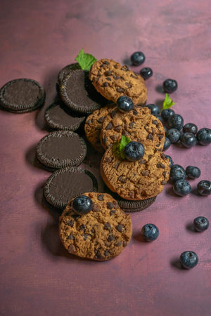 A selection of chocolate and blueberry cookies, with fresh blueberries scattered on a bright and...