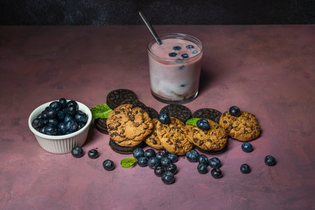 A vibrant, deep purple smoothie in a glass decorated with an orange slice, accompanied by shortbread...