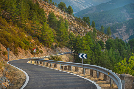A mountain road with sharp turns between rocky canyons where the creeping vegetation creates chromatic contrasts with the multicolored geological formationsの写真素材