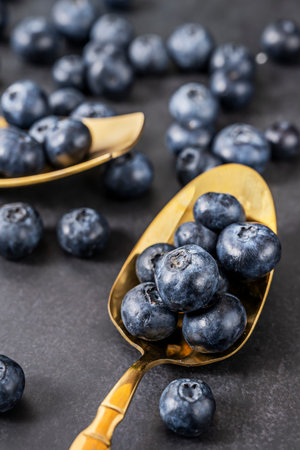 Composition with wild blueberries on a black plush background and a polished brass spoon gently reflecting the lightの写真素材