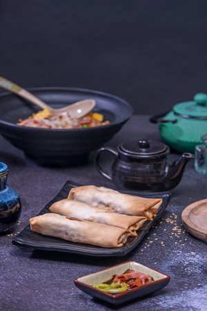 Contemporary still life with freshly fried spring rolls on a rustic wooden board, accompanied by soy...
