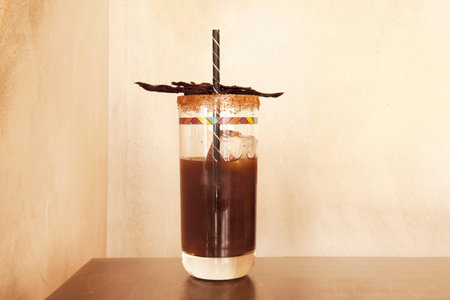 A brown michelada with a straw and pieces of dried meat on a wooden table