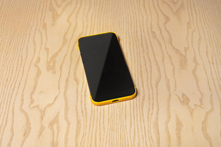 Black and yellow smartphone on a wooden table. Top view. Close-up.