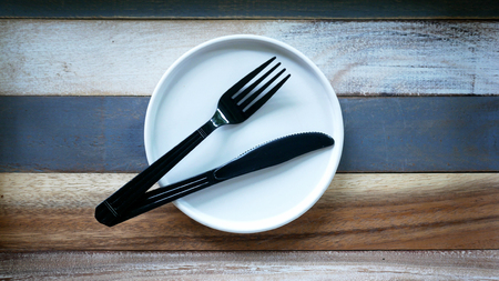 black knife and fork on round white dish,wooden vintage background.の写真素材