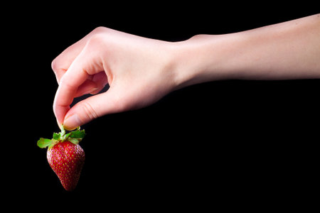 Hand holding a strawberry. Isolated on black.の写真素材