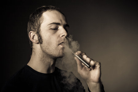 Man smokes electronic cigarette on dark background.