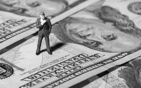 Miniature figurine businessman with 100 dollars banknote on backgroundの写真素材