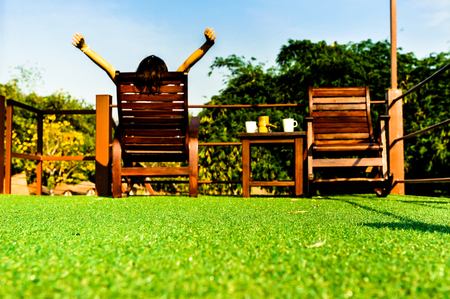woman relaxing on wooden sunbed on green artificial grass and looking the blue sky backgroundの写真素材