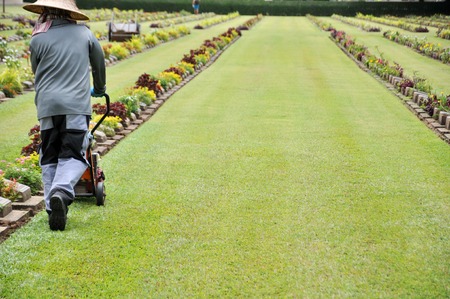 gardener working on the lawn in a cemetery with headstones in the background at Kanchanaburi War Cemetery in Thailand.の写真素材